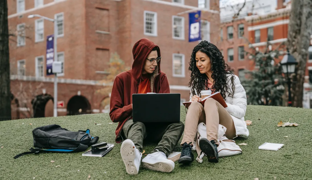 young man and woman sit behind laptop and book outside on college campus