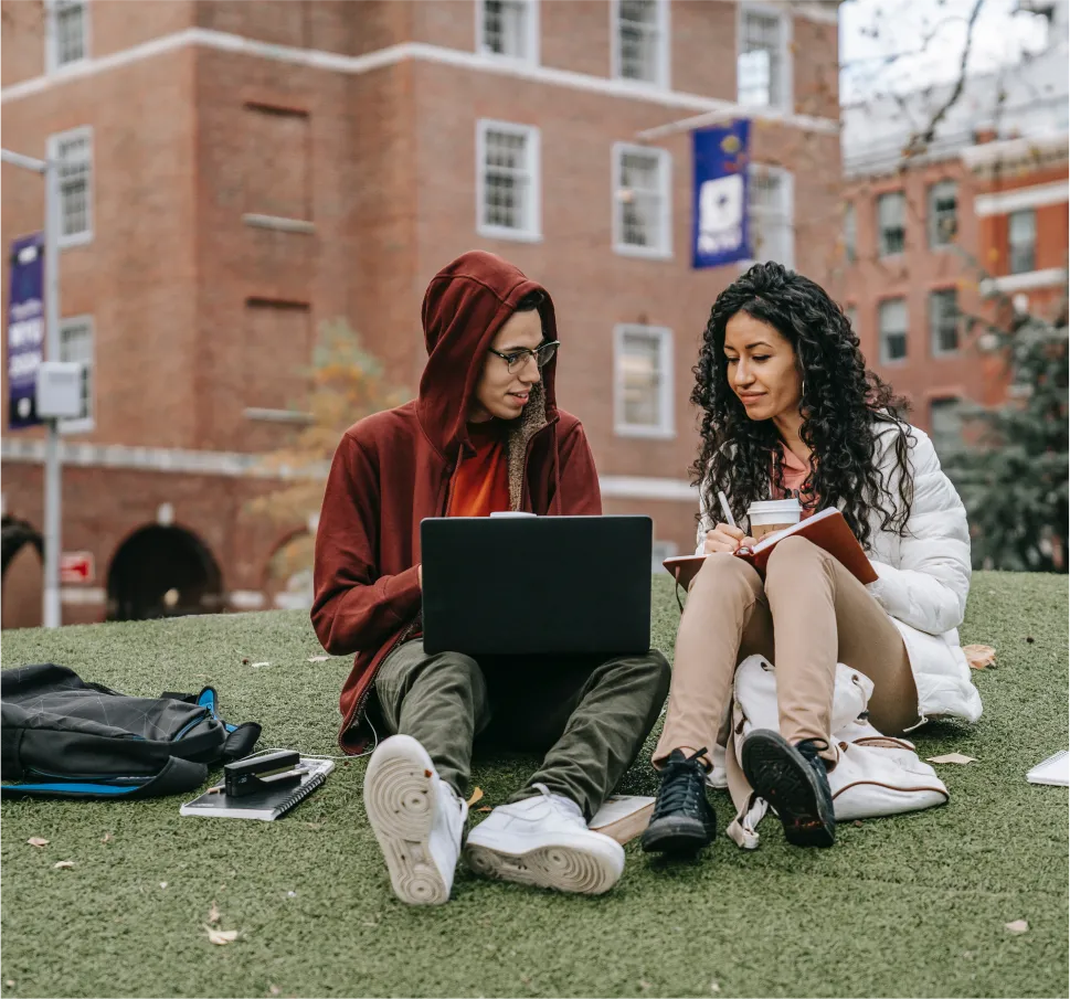 young man and woman sit behind laptop and book outside on college campus