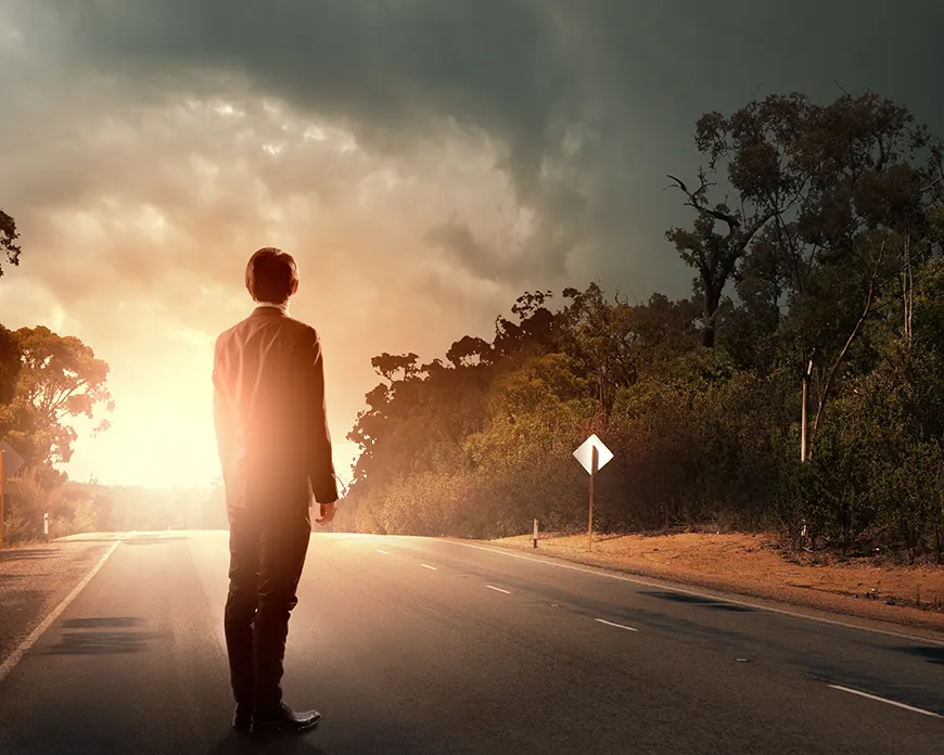 One man standing in the middle of the road looking at a light ahead.