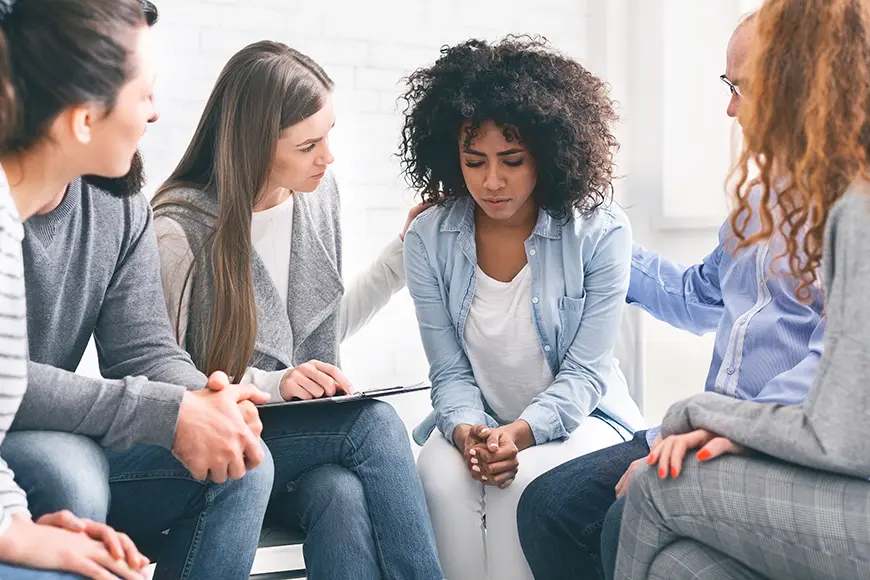 Several people comforting a woman that shows signs of distress.