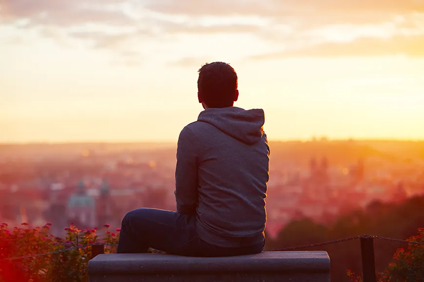 A young man looking at a city at sunset.