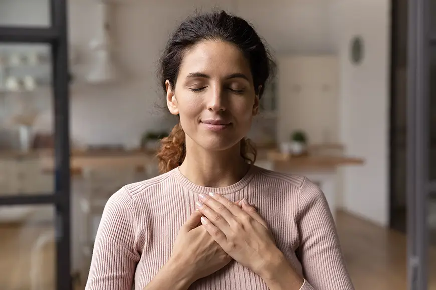 Content woman with eyes closed and hand on chest feels relief from stress