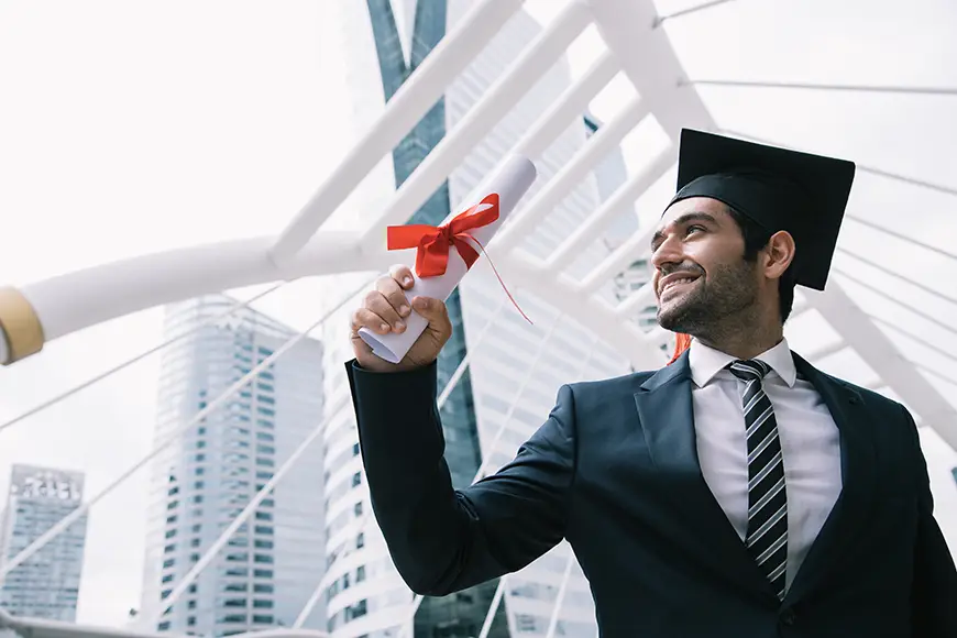 A man in a costume with a graduation hat happily holds his graduation paper.