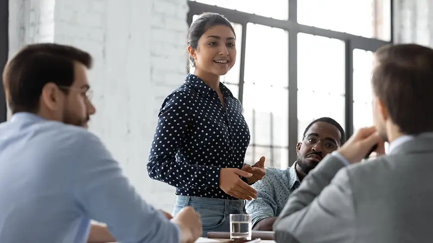 A confident young business leader speaks to a table of her colleagues