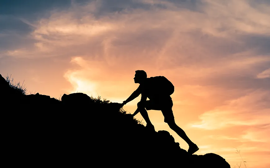 The sunset casting a shadow over a man climbing a mountain.