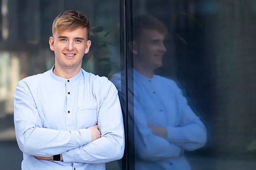 A young leader in formal wear leans against a glass wall