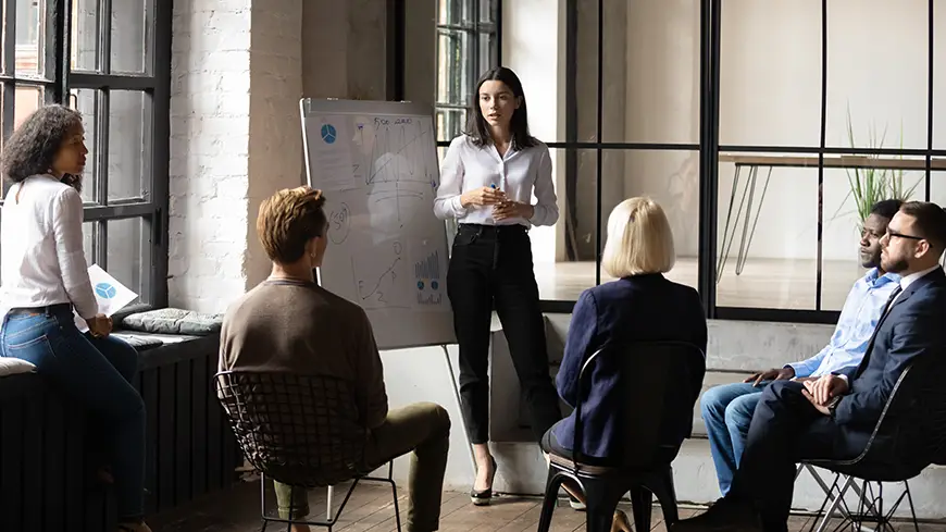 A confident business person stands in front of a whiteboard while briefing their team