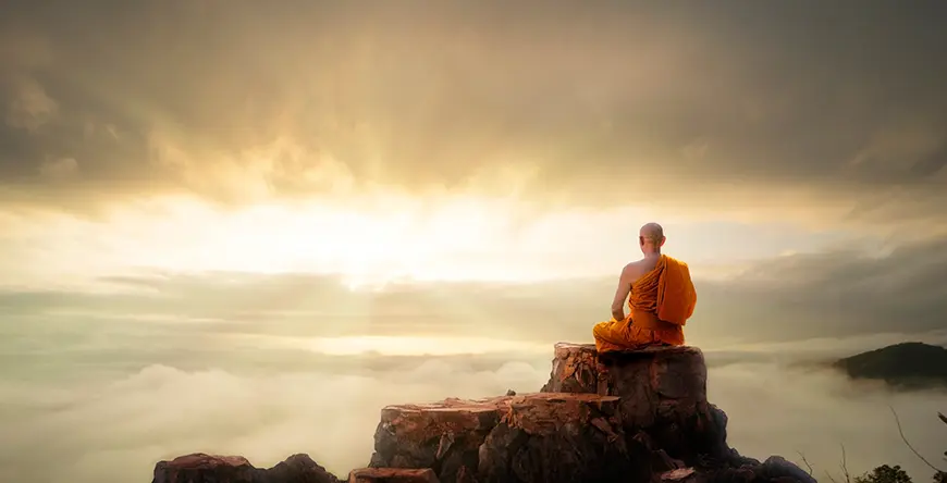 A Buddhist monk sitting on a cliff looking at the clouds