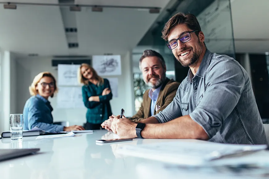 A happy group of people that are working for an enterprise. They are working on a project, smiling, and looking at the camera.