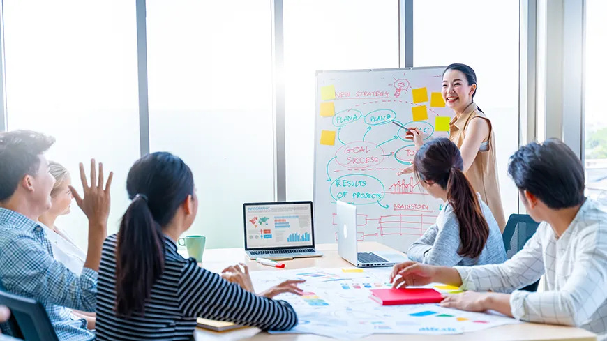 A woman smiles while delivering a presentation filled with charts and graphs in front of a group of professionals.