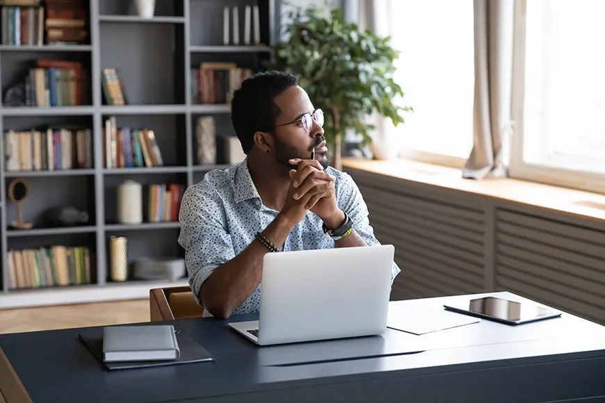 A man in an office space, sitting at his desk, looks outside the window.