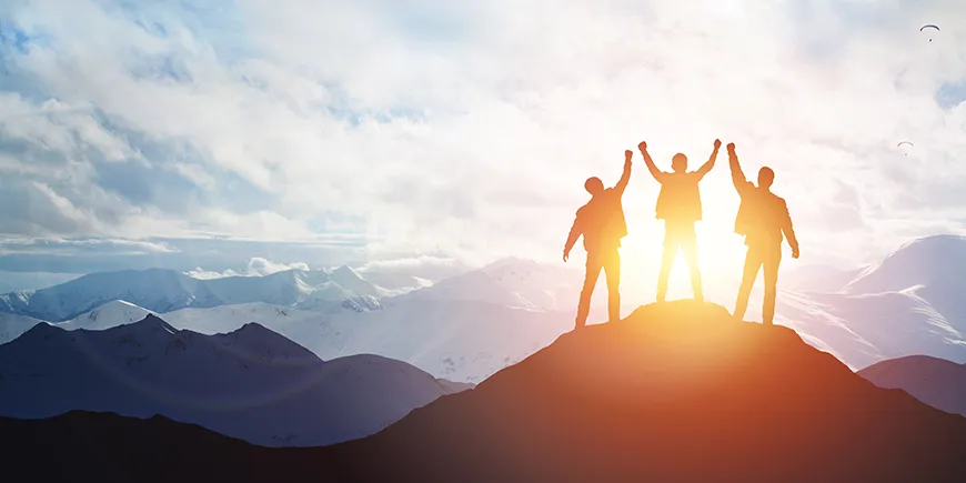 The silhouette of three men standing on the top of a mountain with their arms up above their heads in celebration.