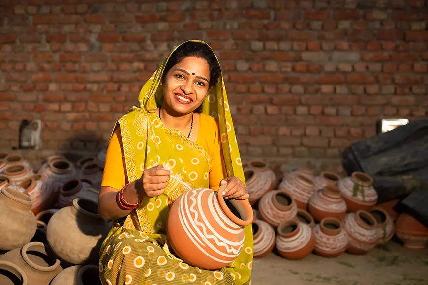 A happy Indian woman works on the decorative design of a clay pot.