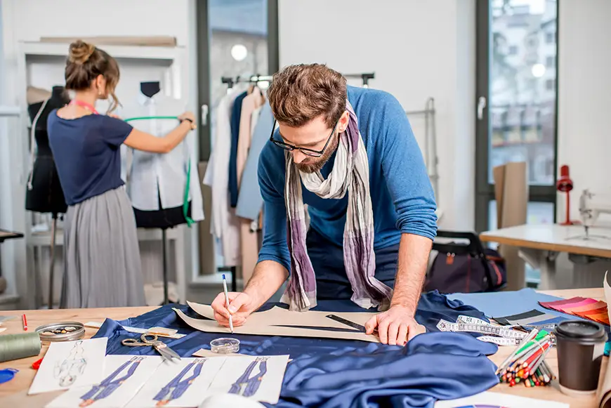 Two fashion designers working with clothing sketches and fabric.