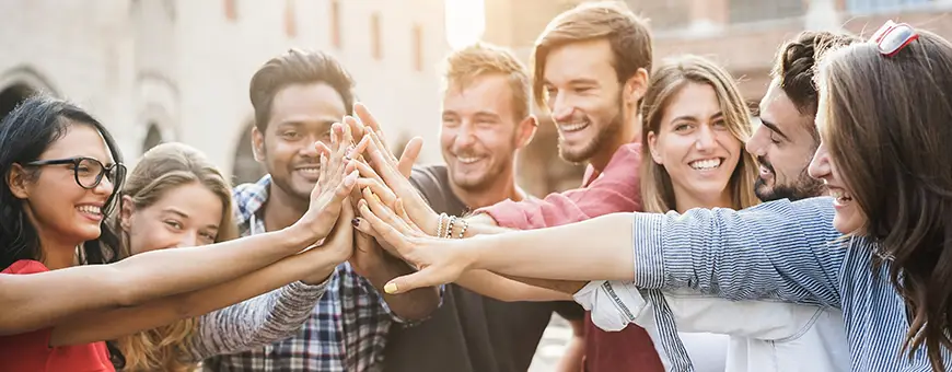 A group of people spanning multiple ethnicities and identities stand in a semicircle and join their hands together at the center.