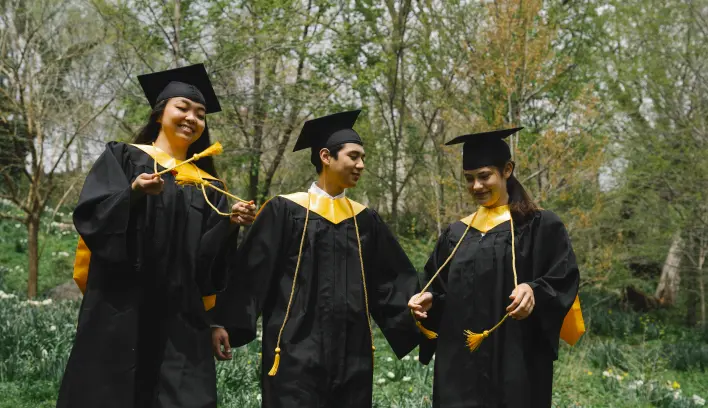 Three new graduate students wearing black caps and gowns smiling and enjoying themselves.