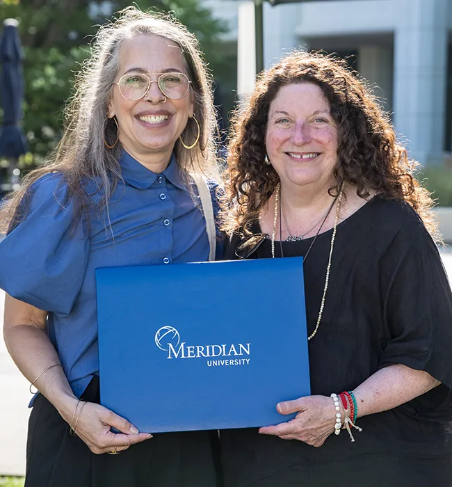 a recent meridian graduate and faculty hold up a meridian diploma