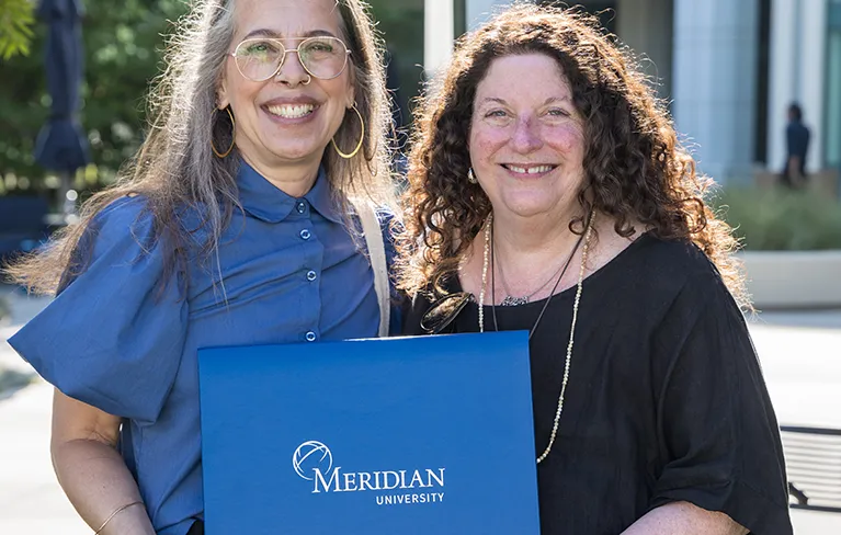 a recent meridian graduate and faculty hold up a meridian diploma
