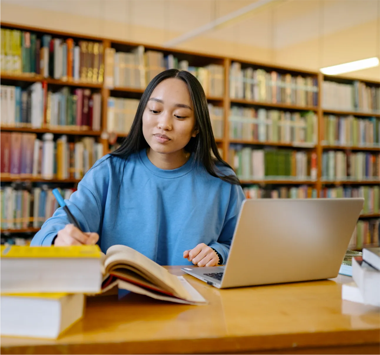 young woman sits behind laptop and book doin research in library